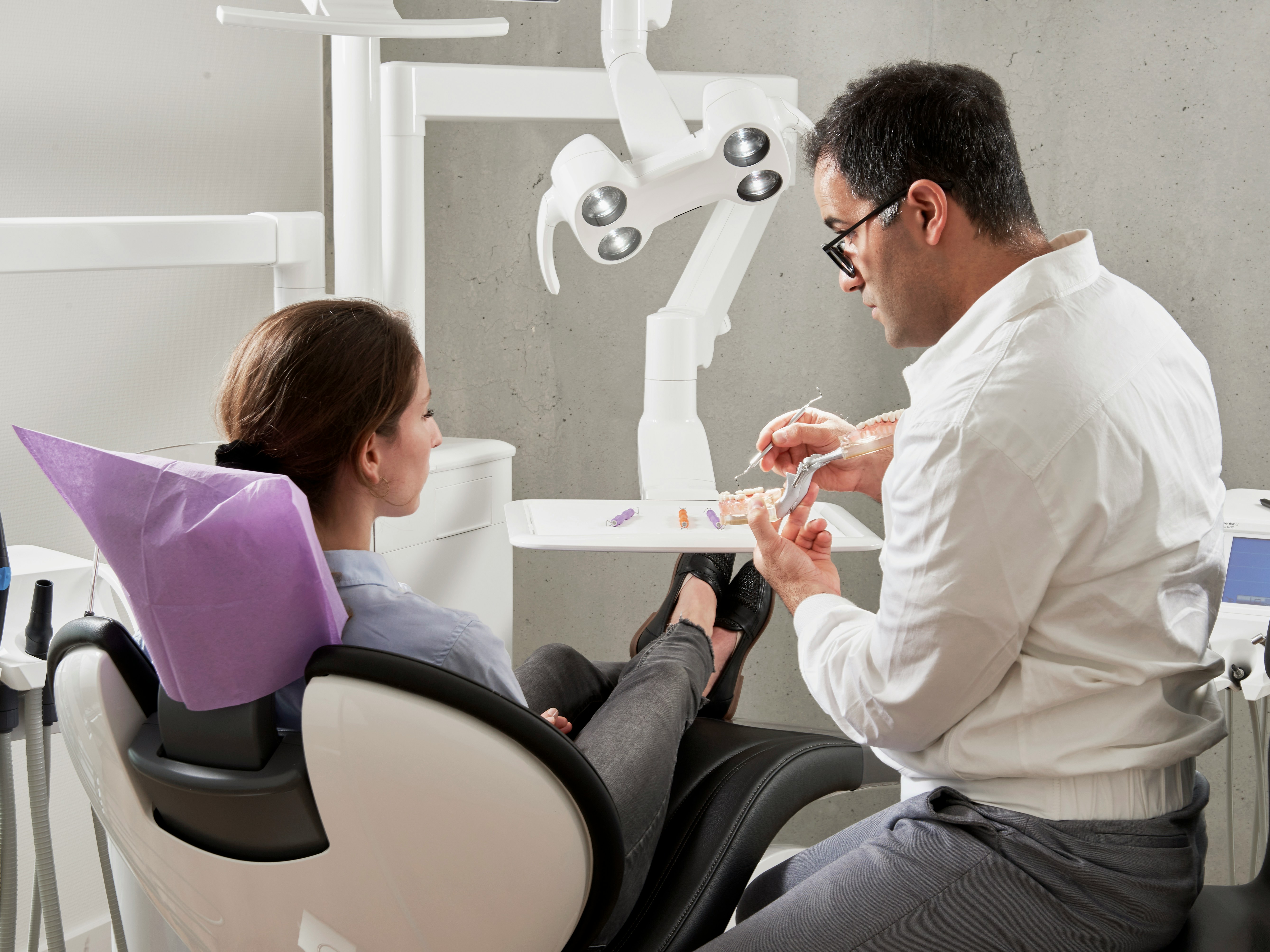 NHS dental practice reception area showing urgent care scheduling board with dentist and patient in consultation room